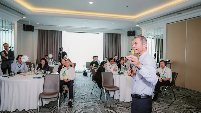 Lecturer presenting before round tables in a CEO Bootcamp 2026 class; attendees wear name tags and interpretation headsets