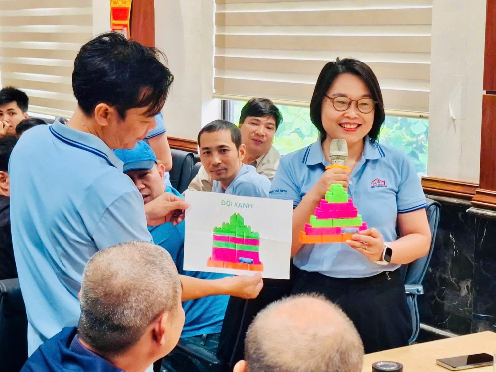 ABC Vietnam team in a workshop: one person holding a sheet printed “ĐỘI XANH”, another holding a microphone and a block model, the group watching