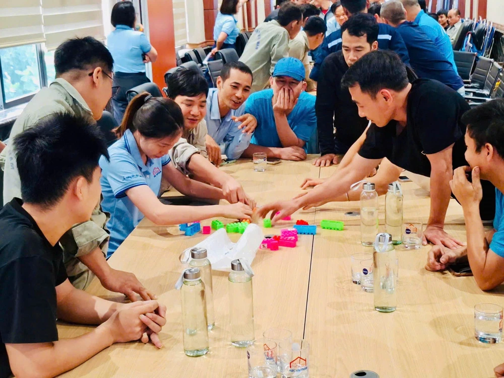 The whole ABC Vietnam team around a table assembling a model from coloured blocks; mugs printed “ABC VIETNAM” on the table